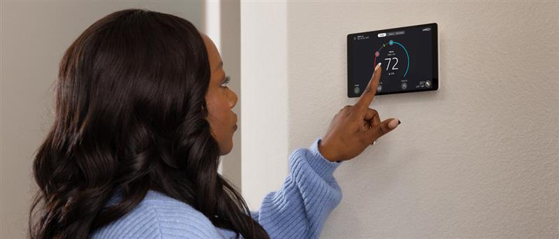 Person adjusting a smart thermostat on a wall, setting temperature to 72 degrees and selecting hold mode