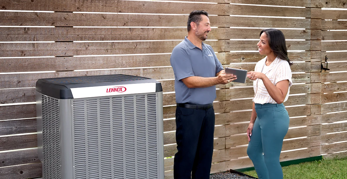 Dealer and homeowner talking beside a Lennox air conditioner installed next to a wooden fence