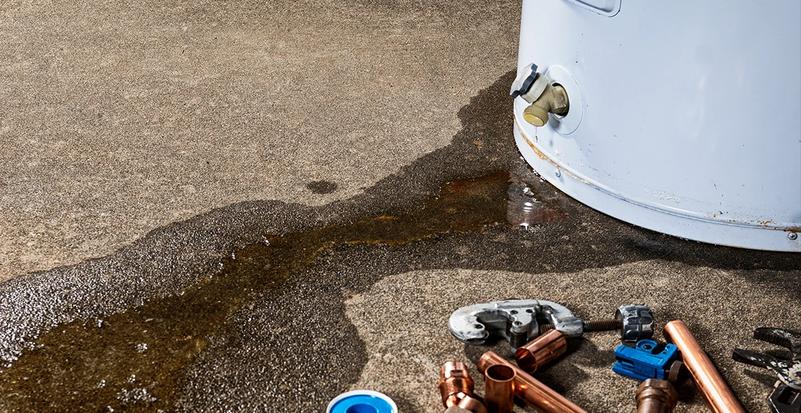 Water heater leaking onto the floor with tools and copper fittings scattered nearby