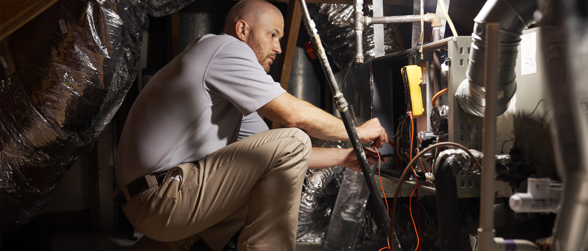 Technician installing a furnace in a residential basement, using tools and diagnostic equipment to connect ducts and wiring.