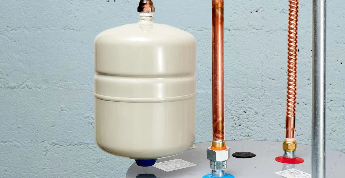 Close-up of a white boiler expansion tank installed above a water heater with copper pipes and fittings