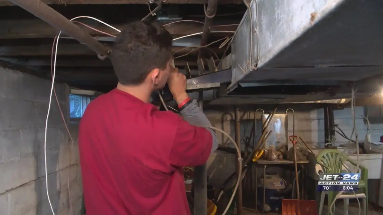 Installer in a red shirt working inside a basement, inspecting or installing HVAC ductwork.